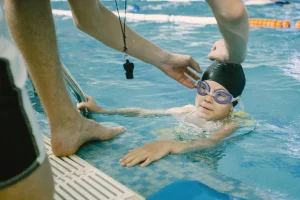 girl-taking-swiming-lesson-male-coach-dad-helping-her-with-goggles-while-swimming